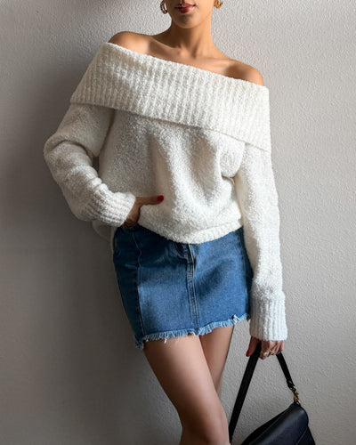 Model wearing the Sydney off-the-shoulder sweater in ivory, featuring a loose fit and relaxed neckline, styled with a denim mini skirt.